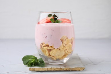 Glass with yogurt, strawberries and corn flakes on white textured table