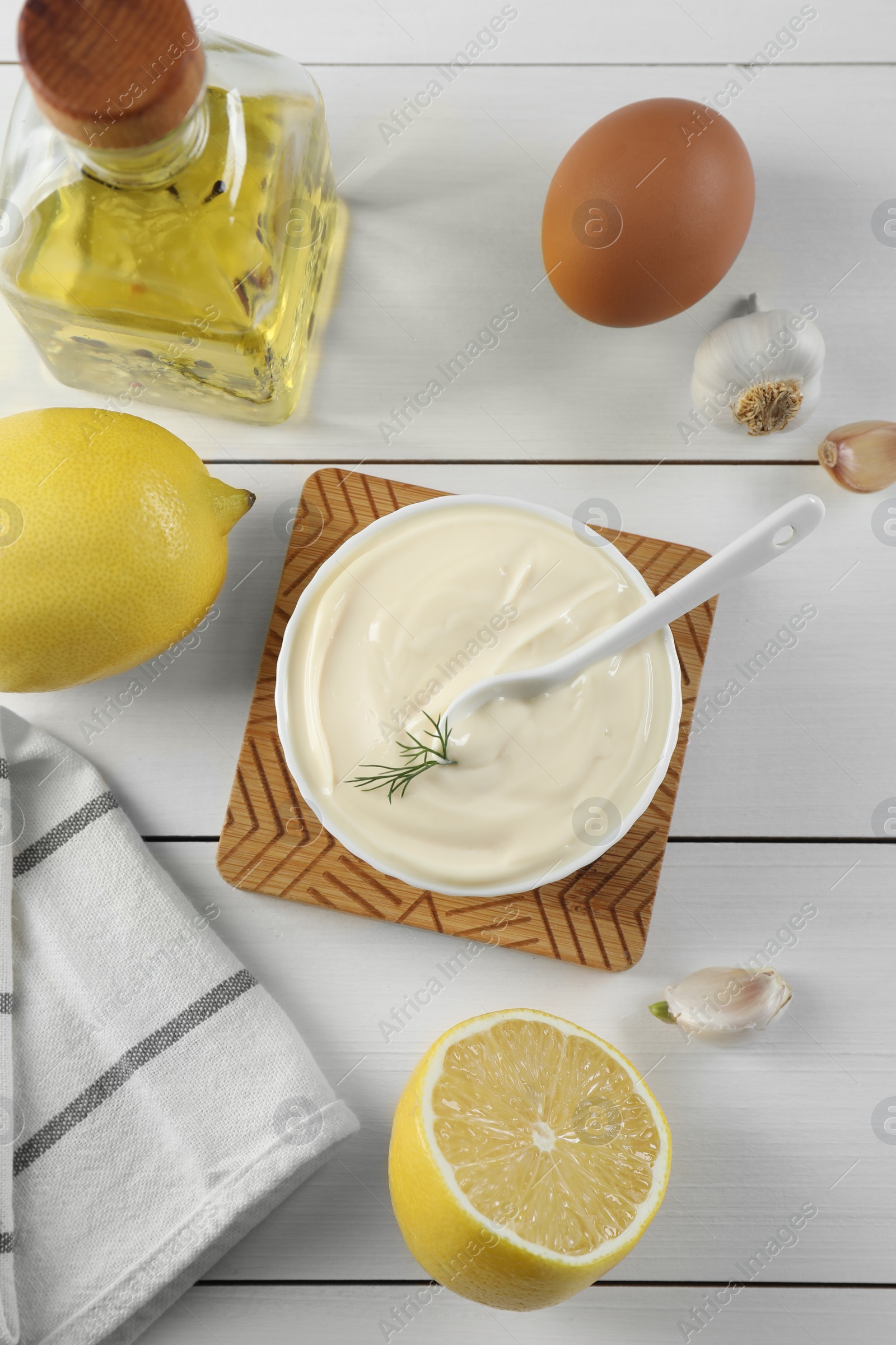 Photo of Fresh mayonnaise sauce in bowl and ingredients on white wooden table, flat lay