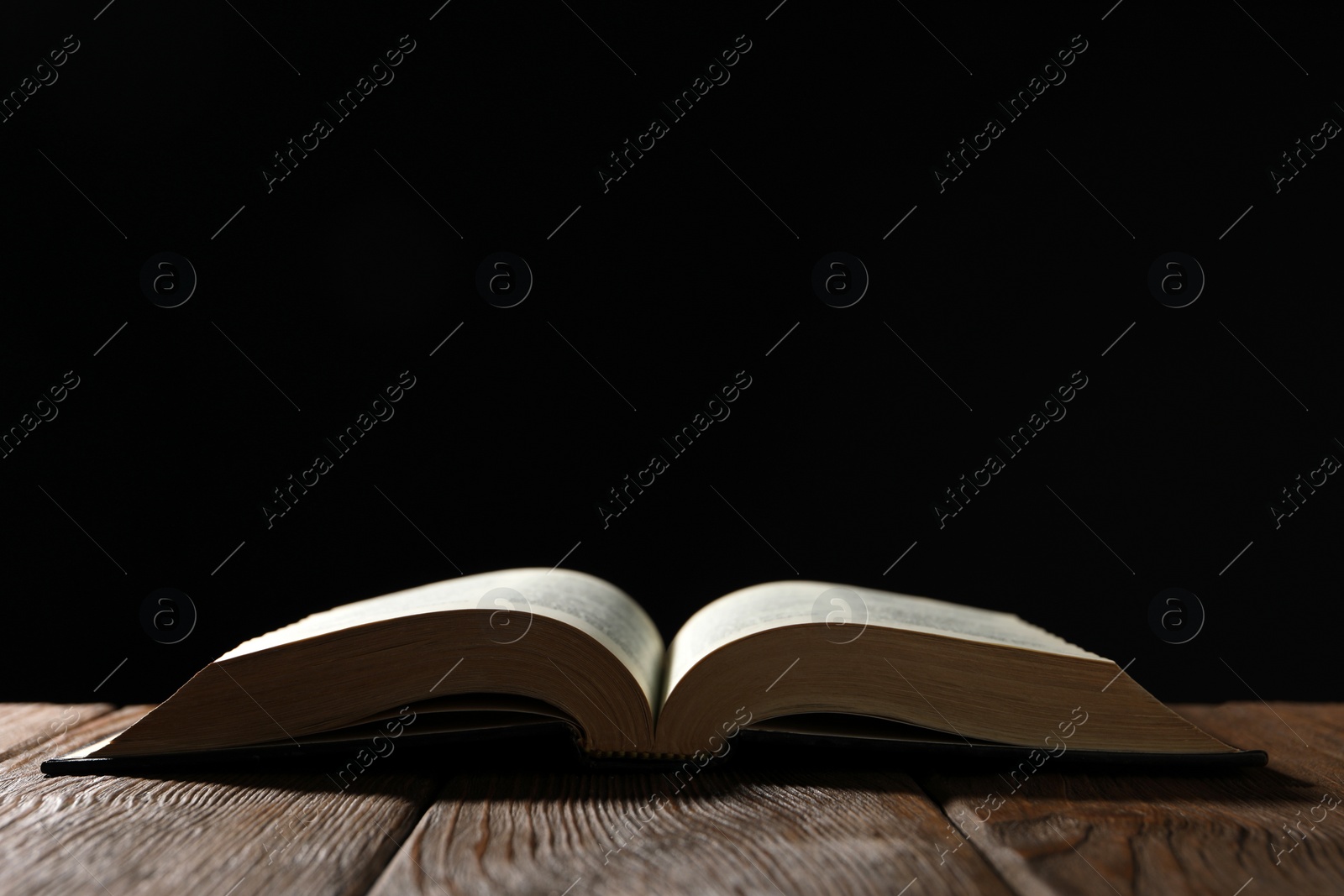 Photo of Open Bible on wooden table against black background. Space for text