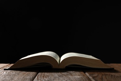 Photo of Open Bible on wooden table against black background. Space for text