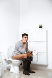 Photo of Man with paper roll sitting on toilet bowl in bathroom