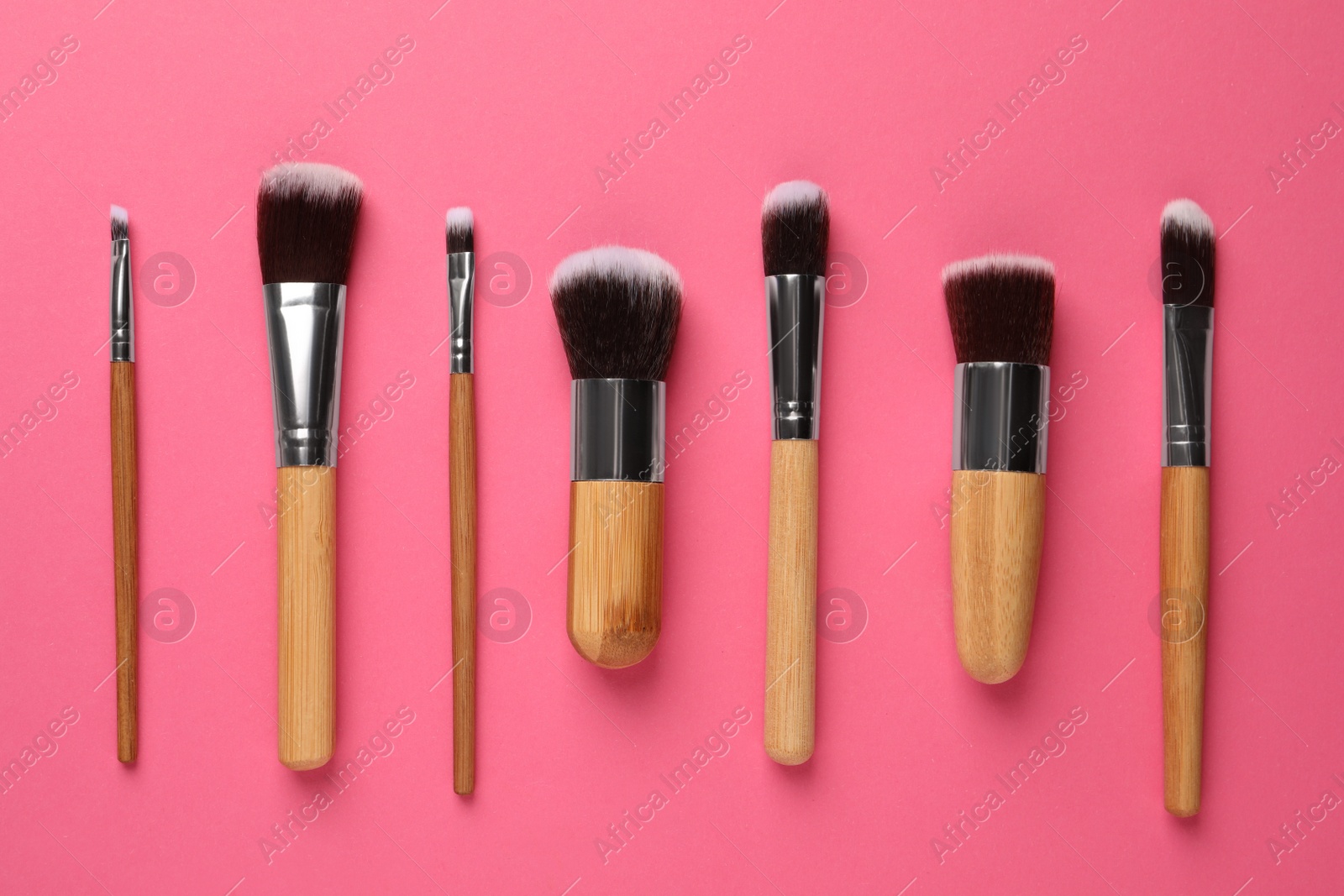 Photo of Set of makeup brushes on pink background, flat lay