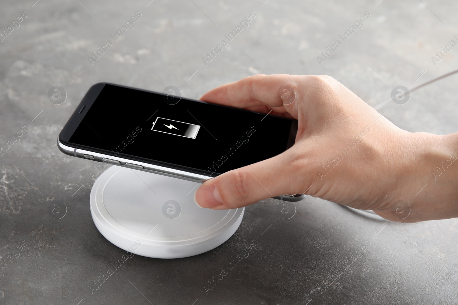 Photo of Woman putting mobile phone onto wireless charger at  grey table, closeup