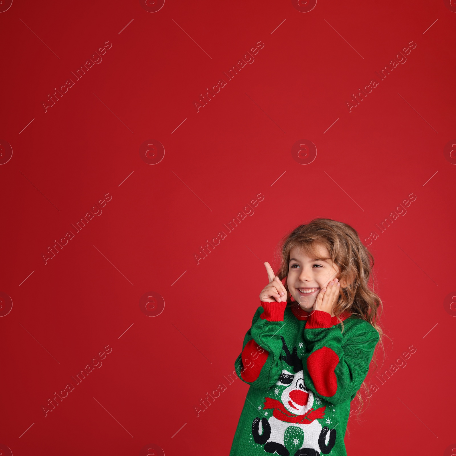 Photo of Cute little girl in green Christmas sweater smiling against red background. Space for text