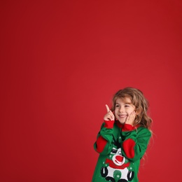 Cute little girl in green Christmas sweater smiling against red background. Space for text