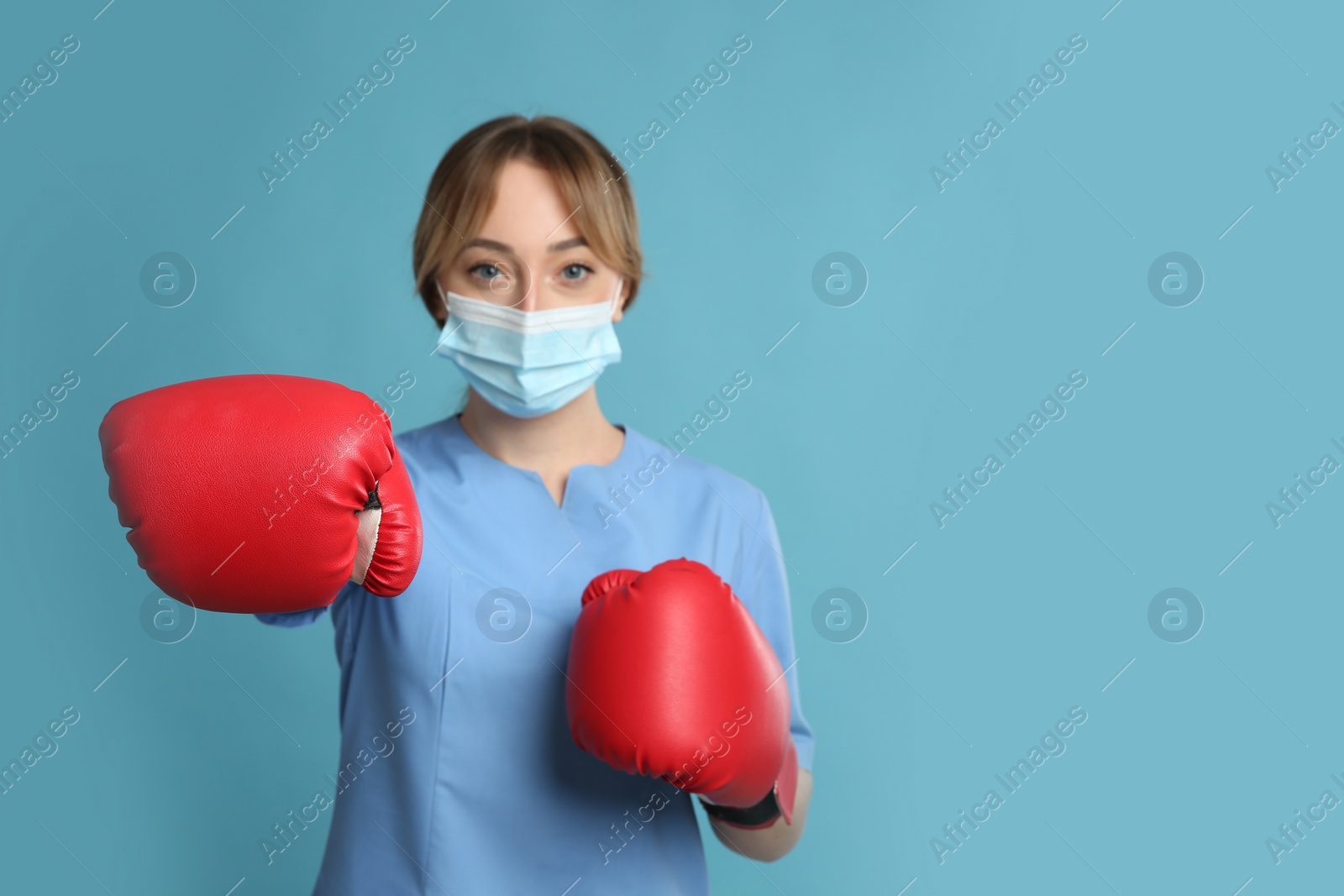 Photo of Doctor with protective mask and boxing gloves on light blue background, space for text. Strong immunity concept