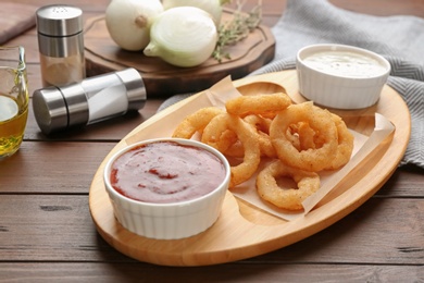 Photo of Plate with fried onion rings and sauces on table