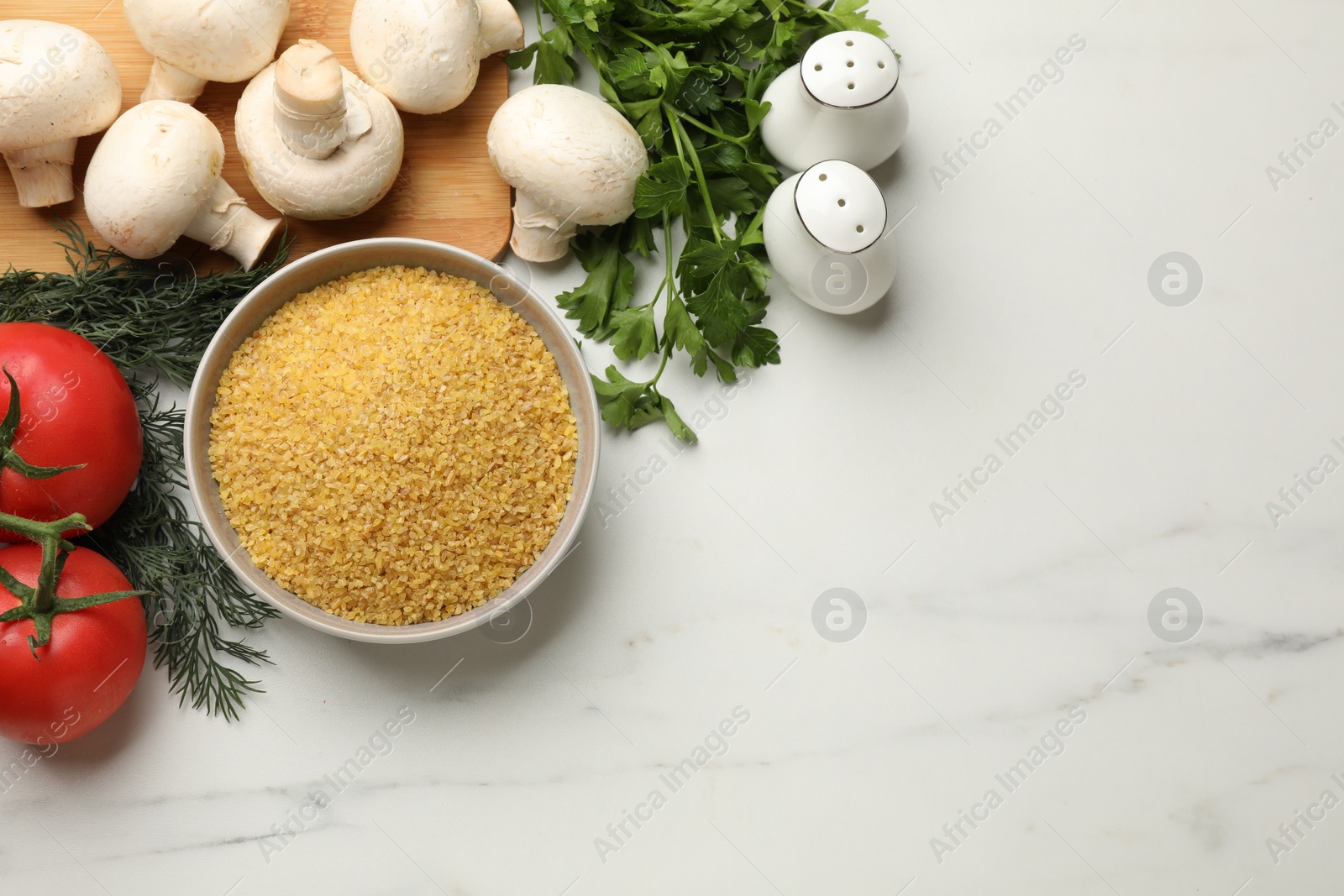 Photo of Raw bulgur in bowl, vegetables and herbs on white table, flat lay. Space for text