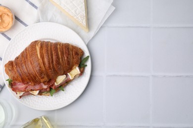 Tasty croissant with brie cheese, ham and bacon on white tiled table, flat lay. Space for text