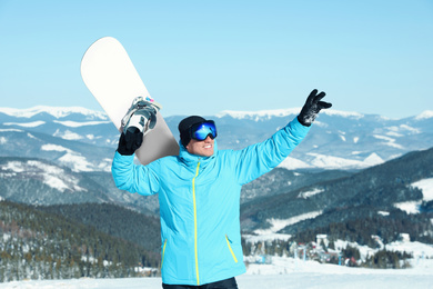 Photo of Happy man with snowboard in mountains. Winter vacation