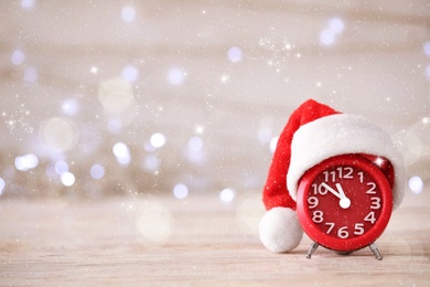 Image of Alarm clock with decor on white wooden table against blurred Christmas lights, bokeh effect. New Year countdown