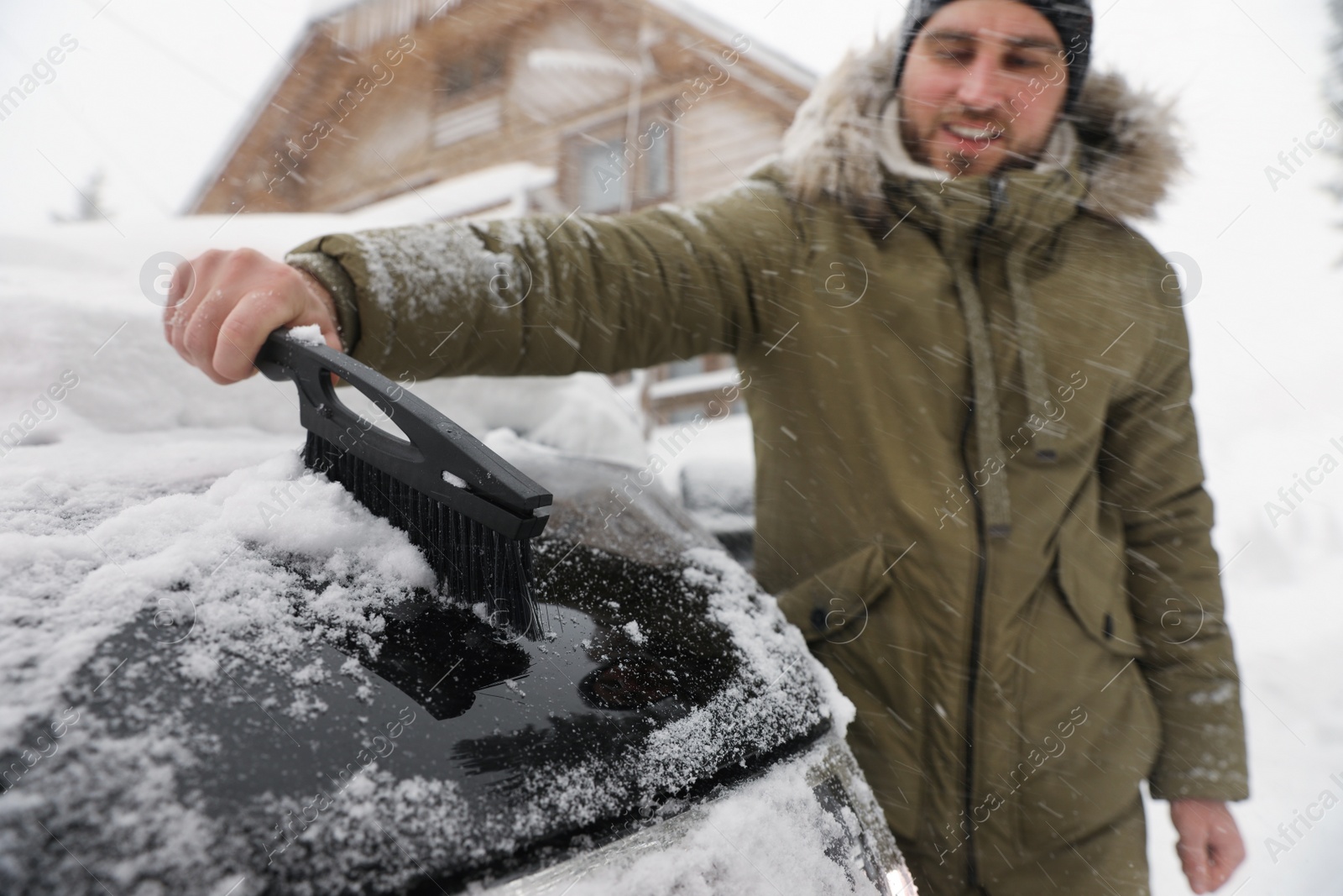 Photo of Young man cleaning snow from car outdoors on winter day