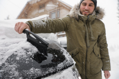 Photo of Young man cleaning snow from car outdoors on winter day