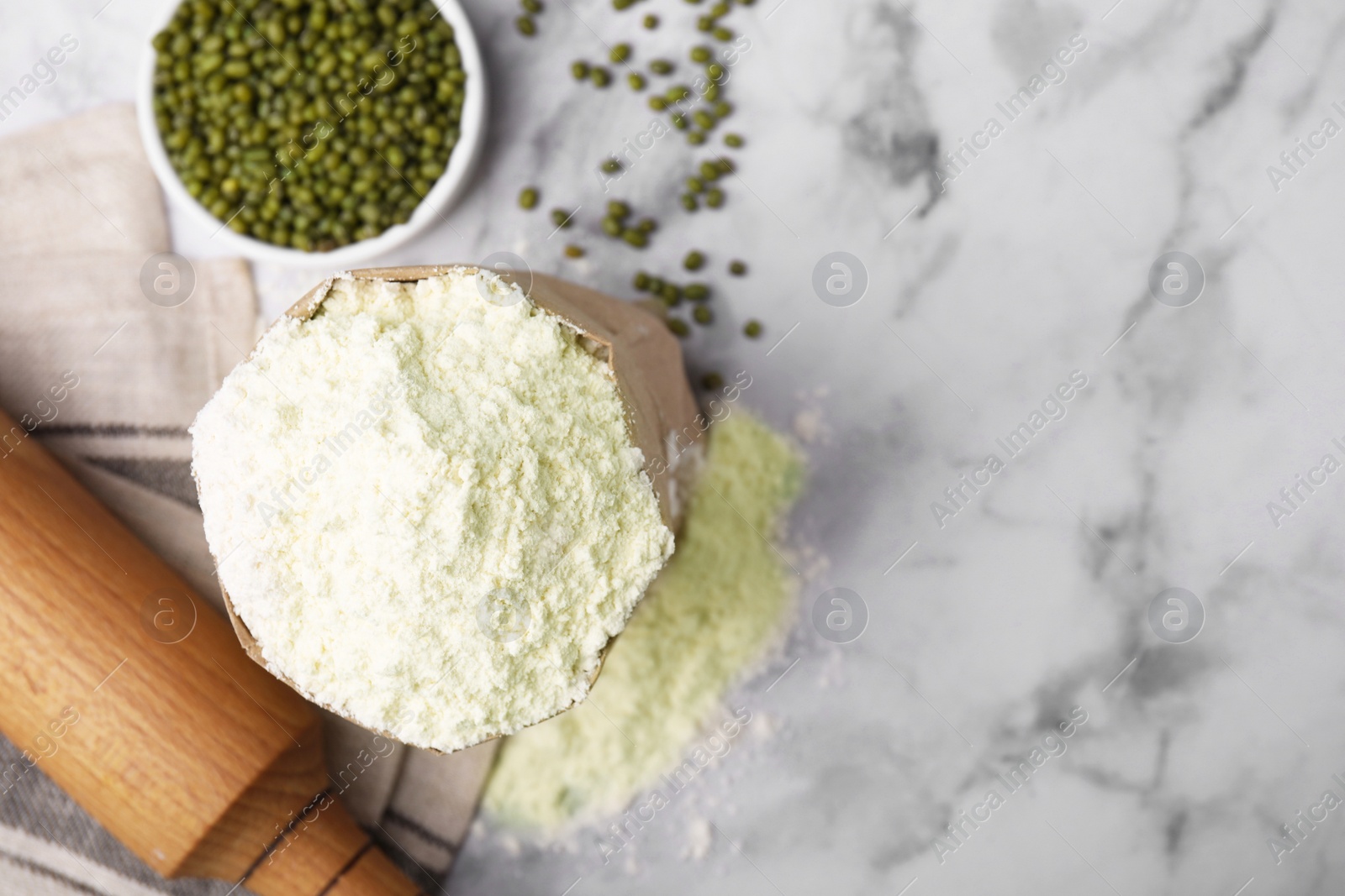 Photo of Mung bean flour in paper bag and seeds on white marble table, flat lay. Space for text