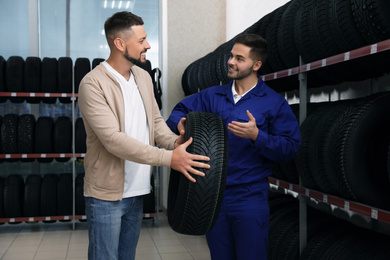 Mechanic helping client to choose car tire in auto store