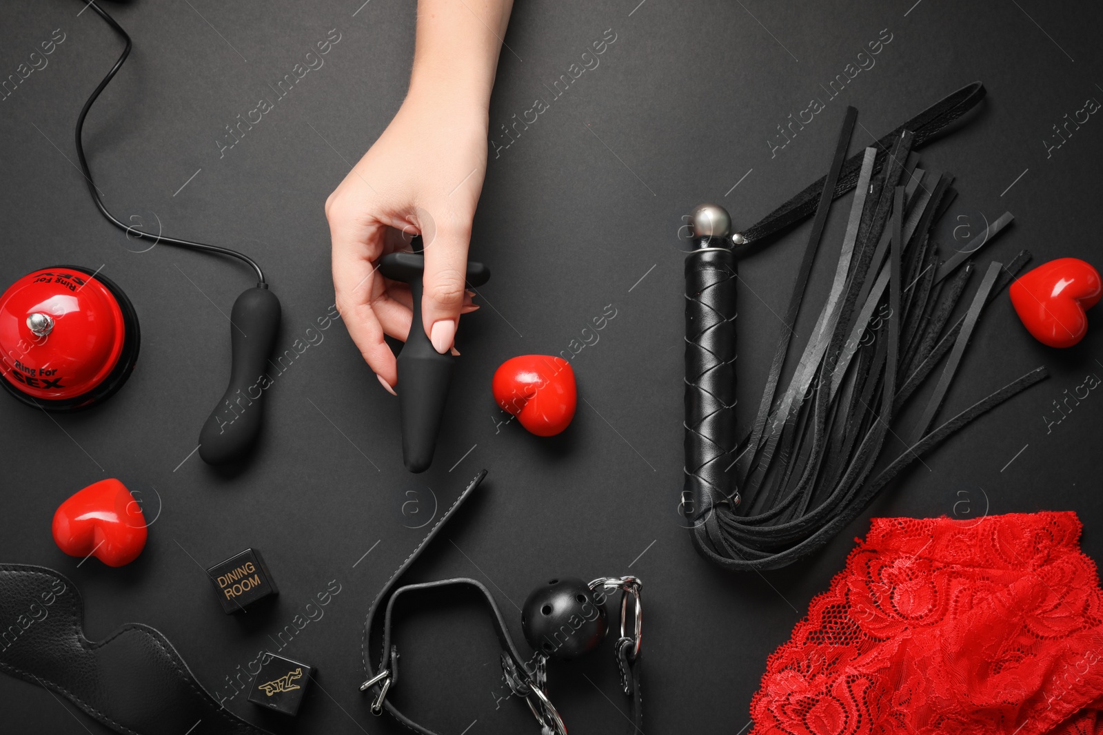 Photo of Woman holding anal plug near sex toys on black background, top view