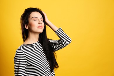 Portrait of young woman with beautiful black hair on yellow background, space for text