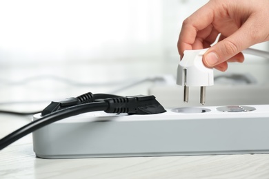 Photo of Woman inserting power plug into extension cord on floor indoors, closeup with space for text. Electrician's professional equipment