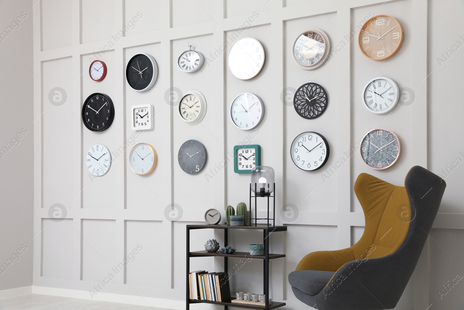 Photo of Armchair, console table and many different clocks hanging on white wall in room