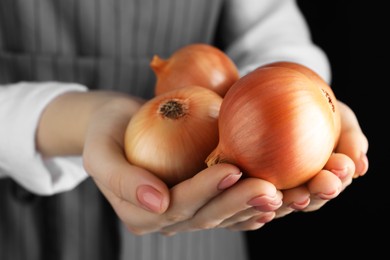 Photo of Woman holding ripe onions on black background, closeup