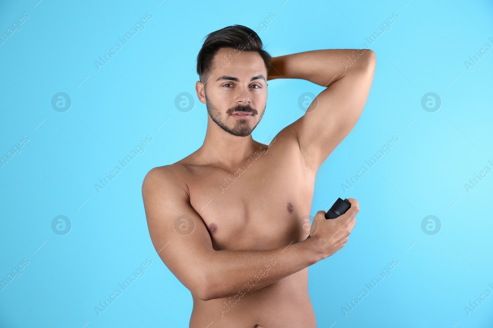 Photo of Young man using deodorant on color background