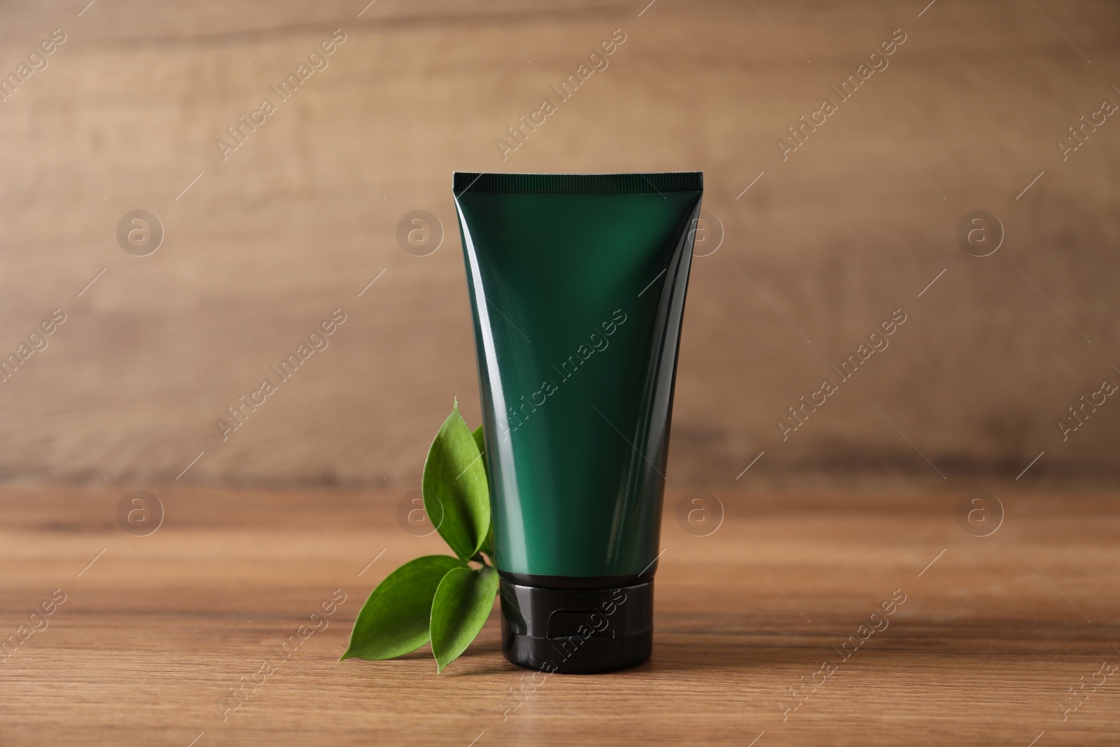 Photo of Tube of men's facial cream and green leaves on wooden table. Mockup for design