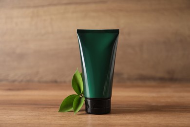 Photo of Tube of men's facial cream and green leaves on wooden table. Mockup for design