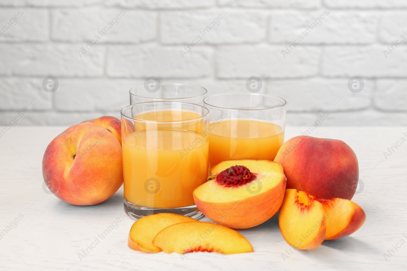 Photo of Glasses of delicious peach juice and fresh fruits on white wooden table