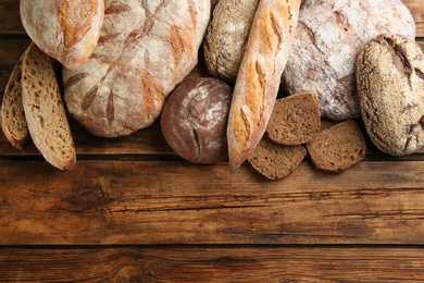 Different kinds of fresh bread on wooden table, flat lay. Space for text