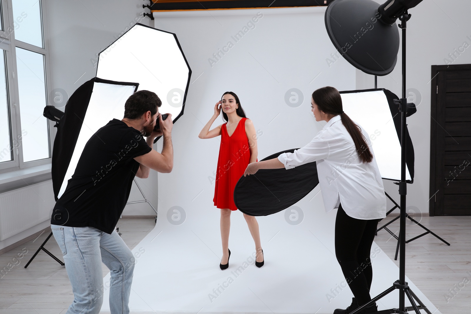 Photo of Professional photographer and assistant working with beautiful model in modern photo studio