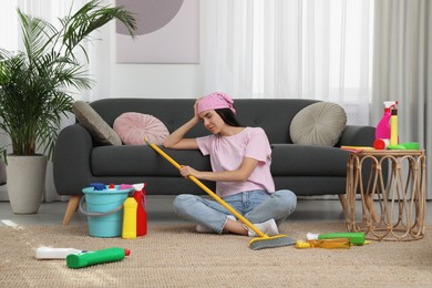Photo of Tired young woman sitting on floor and cleaning supplies in living room