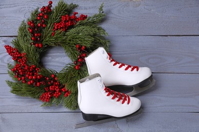 Photo of Pair of ice skates and Christmas wreath on grey wooden background, flat lay