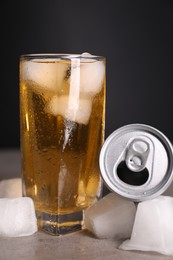 Photo of Tasty energy drink with ice cubes in glass and aluminium can on grey table, closeup