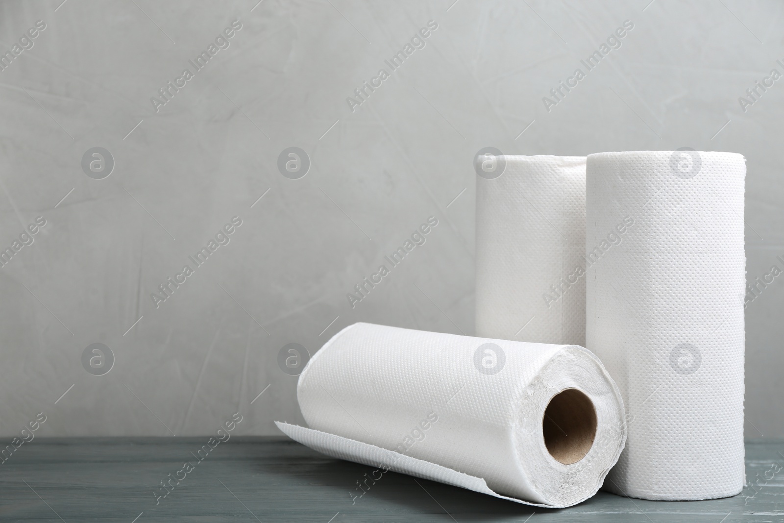 Photo of Rolls of paper towels on grey wooden table, space for text