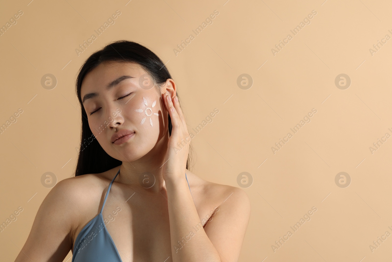 Photo of Beautiful young woman with sun protection cream on her face against beige background, space for text