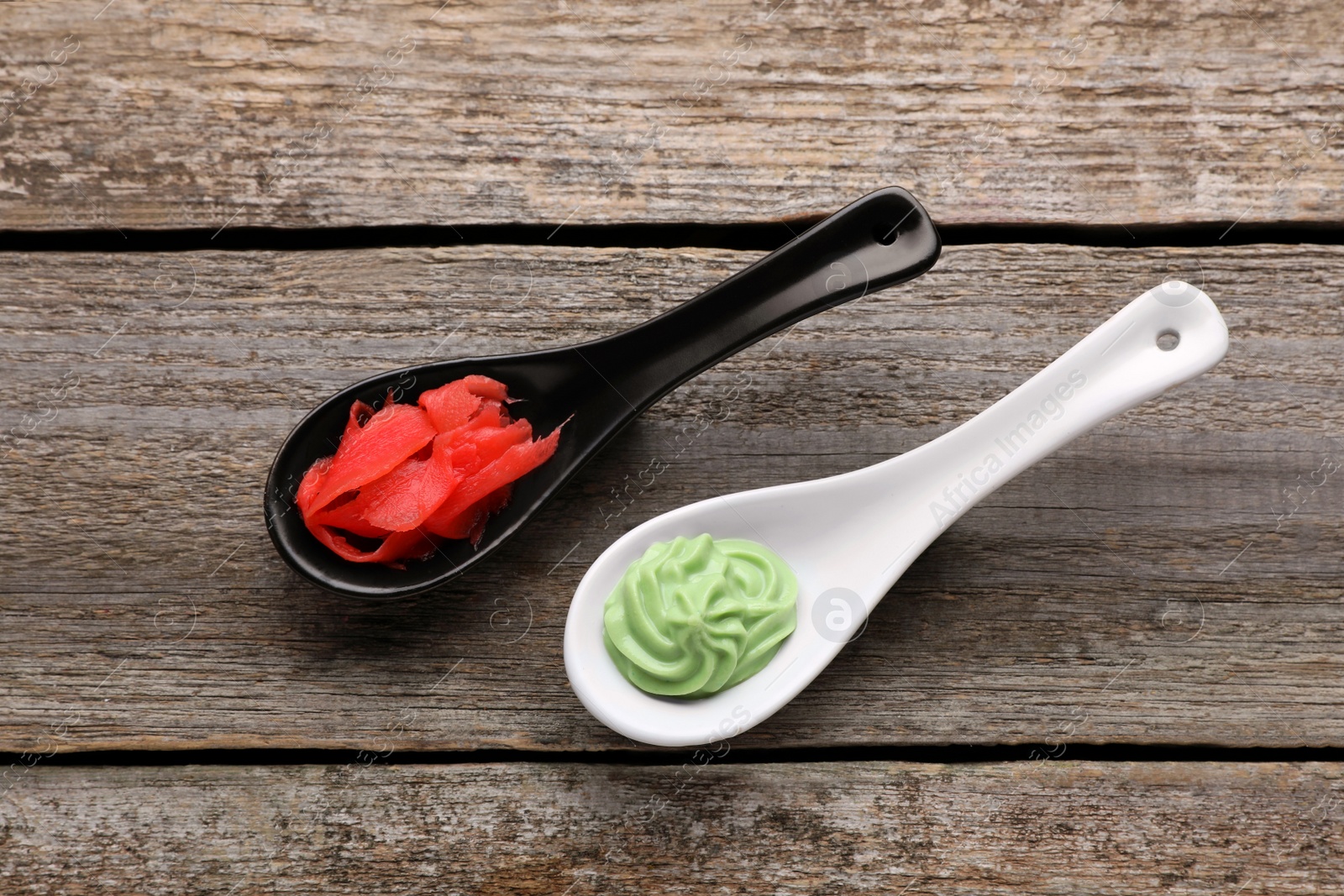 Photo of Spoons with swirl of wasabi paste and pickled ginger on wooden table, flat lay