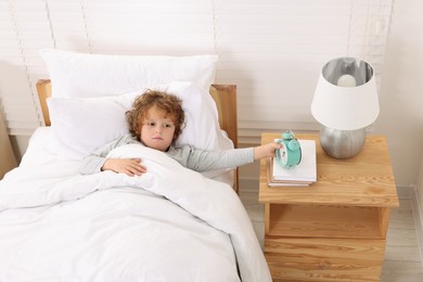 Frustrated boy with alarm clock in bedroom