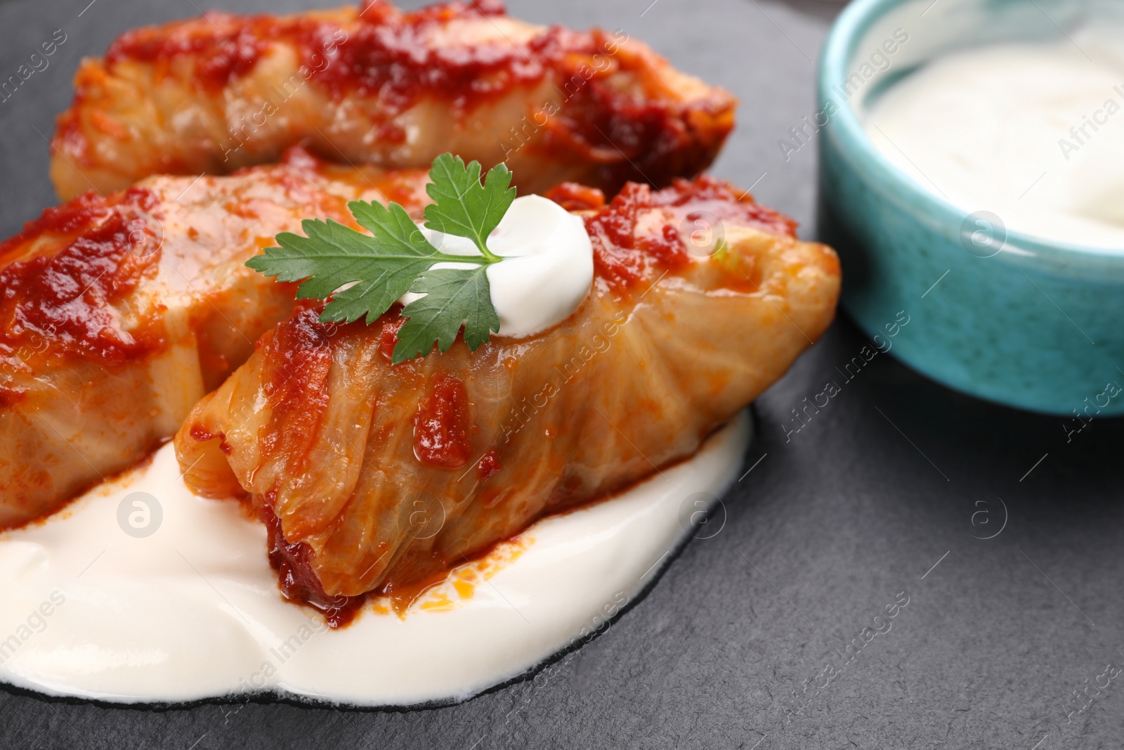 Photo of Delicious stuffed cabbage rolls served with sour cream on slate plate, closeup