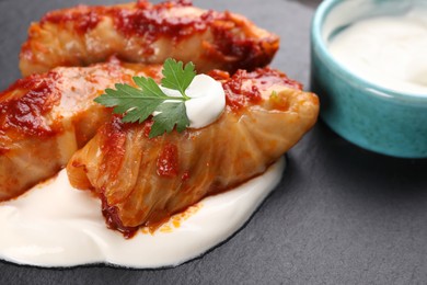 Photo of Delicious stuffed cabbage rolls served with sour cream on slate plate, closeup