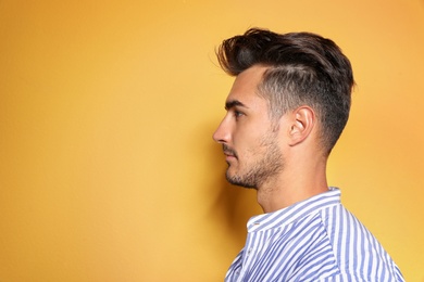 Young man with trendy hairstyle posing on color background