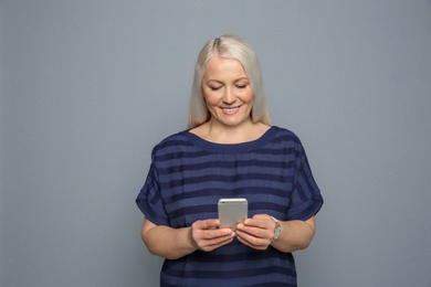 Photo of Mature woman using mobile phone on grey background