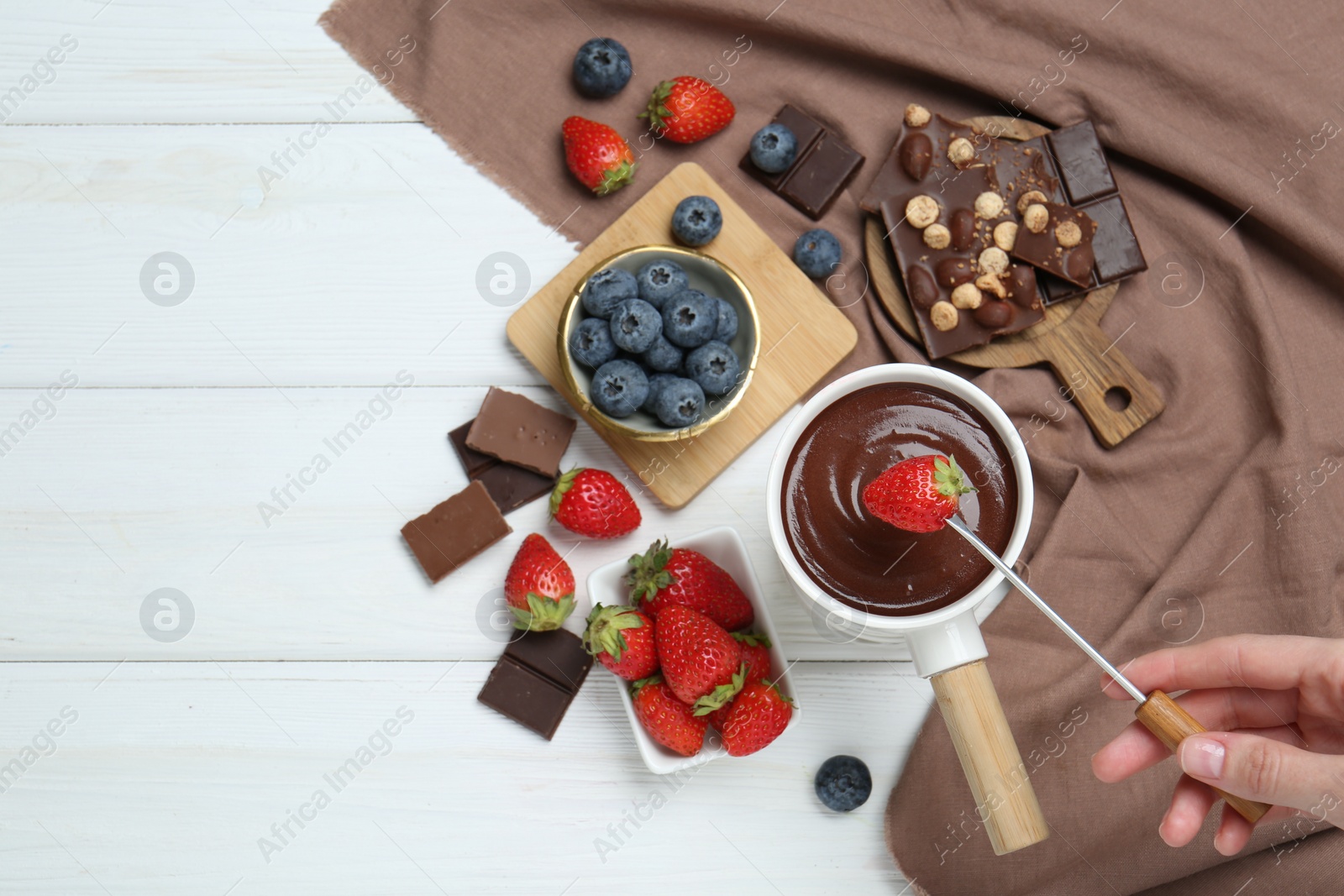 Photo of Woman dipping fresh strawberry in fondue pot with melted chocolate at white wooden table, top view. Space for text