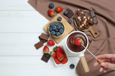 Photo of Woman dipping fresh strawberry in fondue pot with melted chocolate at white wooden table, top view. Space for text