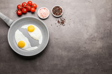 Frying pan with tasty cooked eggs and cherry tomatoes on grey table, flat lay. Space for text