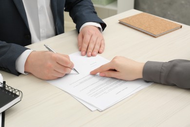 Photo of Woman pointing at document and man putting signature at wooden table, closeup