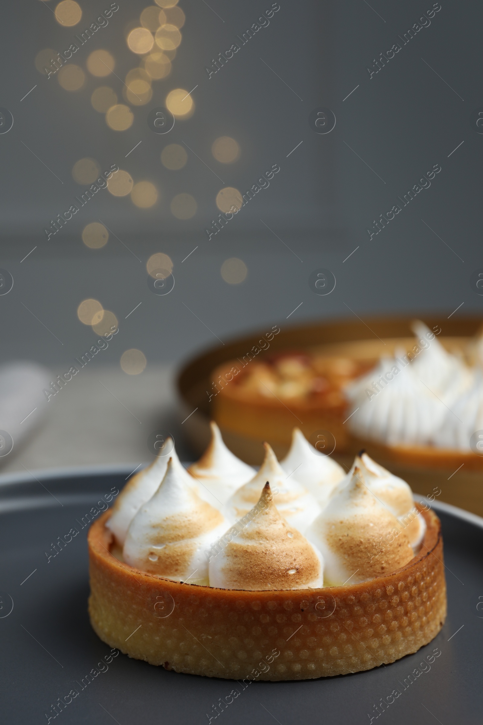 Photo of Tartlet with meringue on table against blurred festive lights, closeup. Delicious dessert