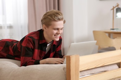 Online learning. Smiling teenage boy with laptop on bed at home