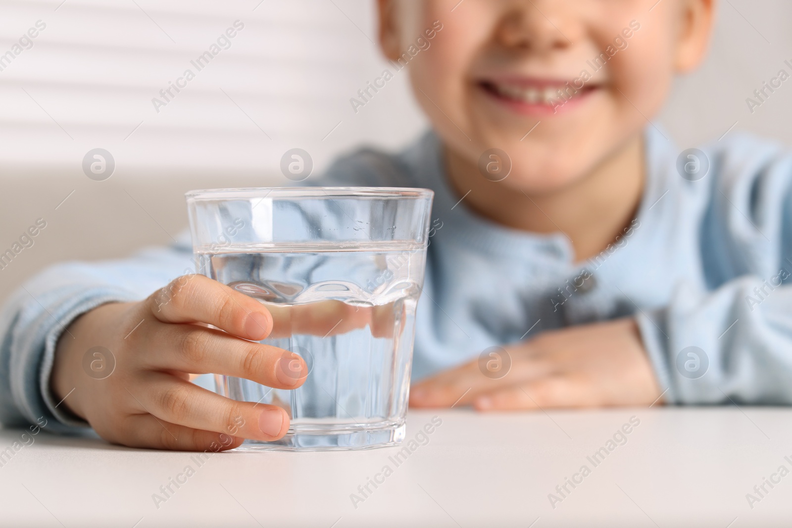 Photo of Little girl holding glass of fresh water at white table indoors, closeup