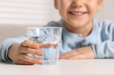 Photo of Little girl holding glass of fresh water at white table indoors, closeup