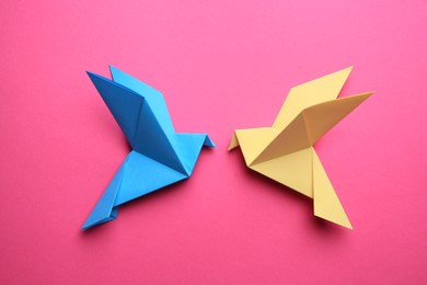 Beautiful colorful origami birds on pink background, flat lay